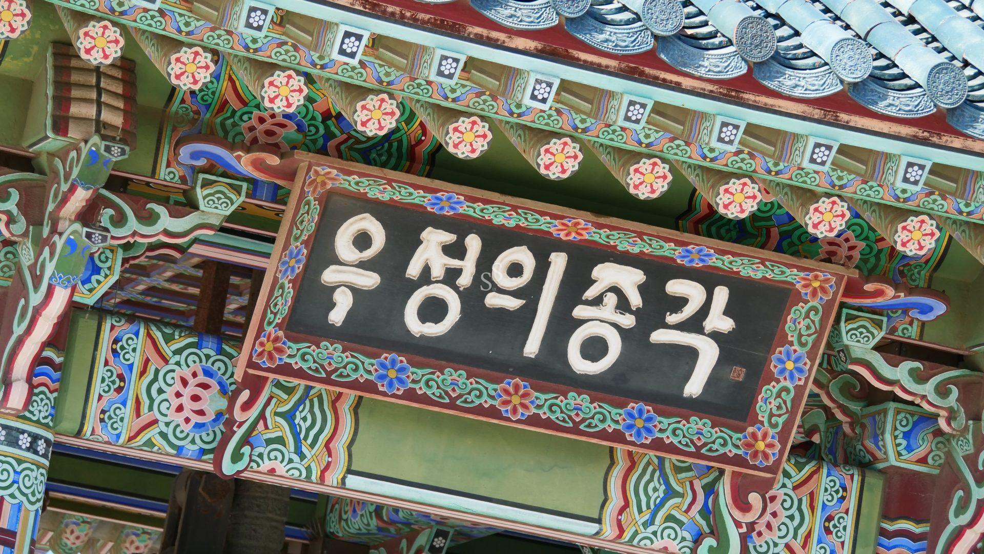 A close-up of a traditional Korean temples ornate wooden structure with colorful painted patterns and a large signboard displaying Korean characters.