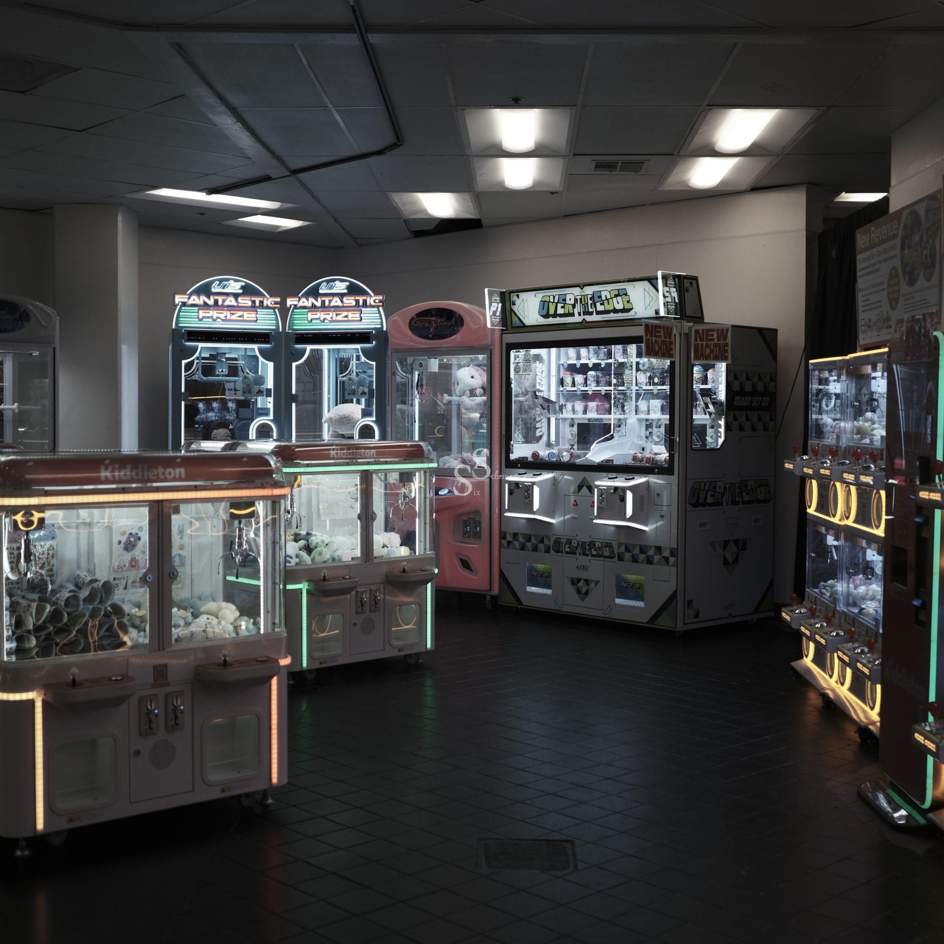 A dimly lit arcade with several claw machines and prize games, glowing with neon lights. The machines are filled with plush toys and prizes, and the room has a dark tiled floor and white ceiling panels.
